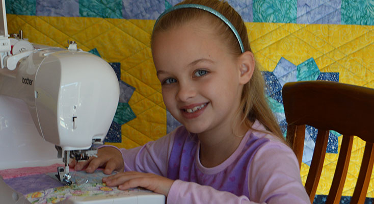 Scarlett Lewis working with her new Brother sewing machine with here 2015 quilt in the background.