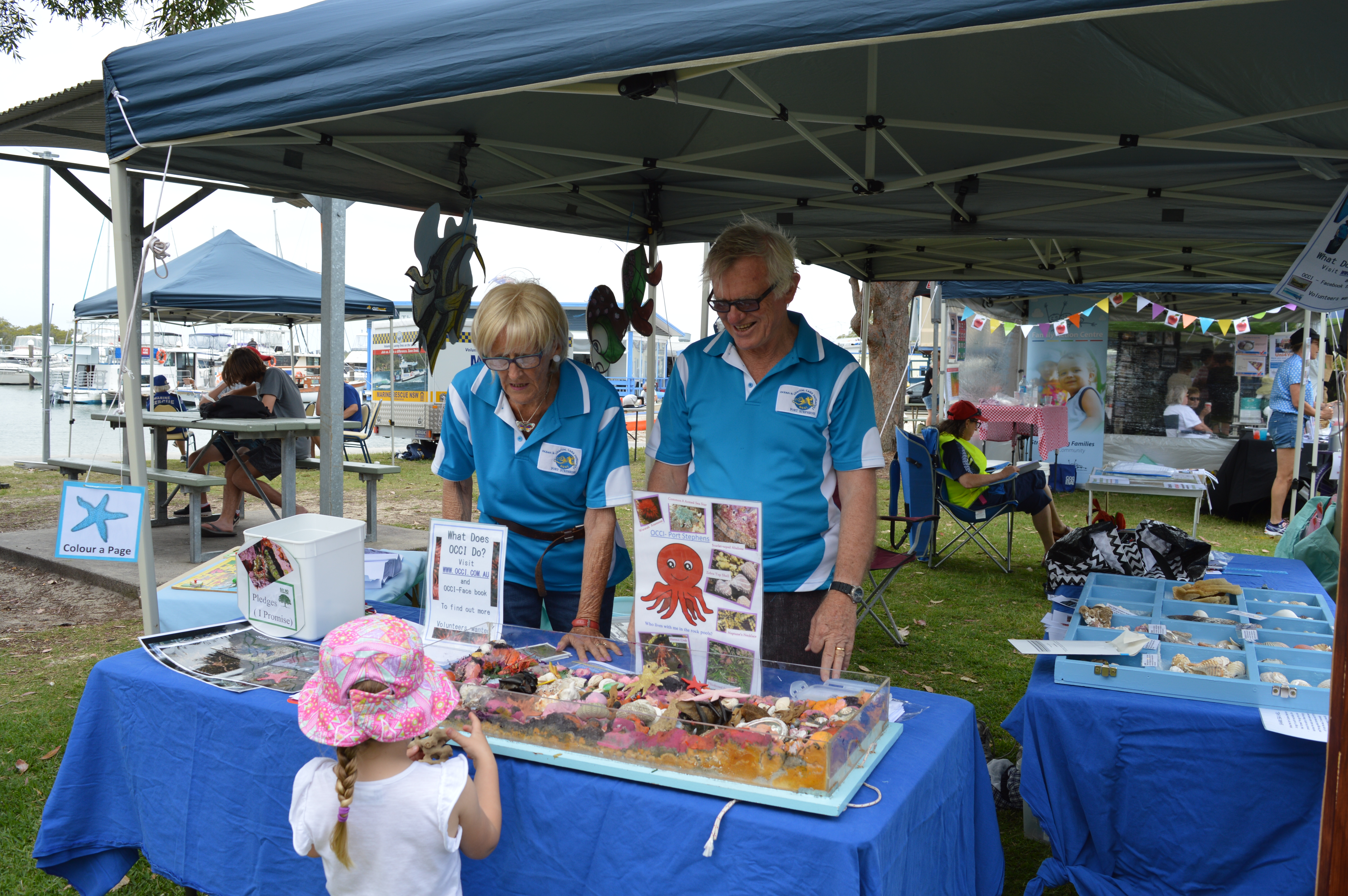 Ainsley and Roger Reeder for OCCI Ocean and Coastal Care Initiatives teach Medowie local, Elizabeth Kilday, 3, about rock pool environments.