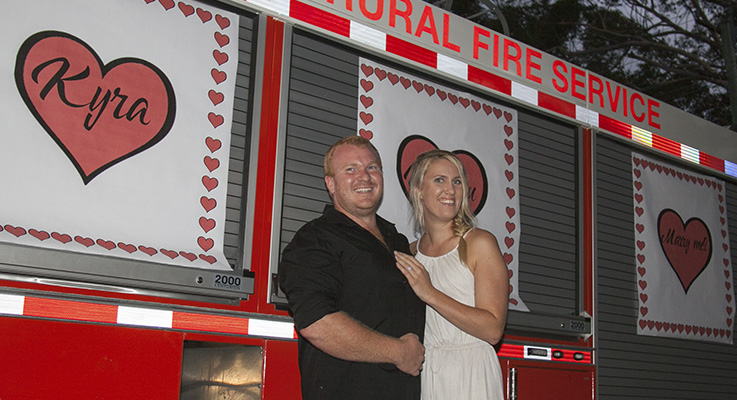 Harrison and Kyra in front of a brigade truck emblazoned with ‘Kyra will you marry me”.
