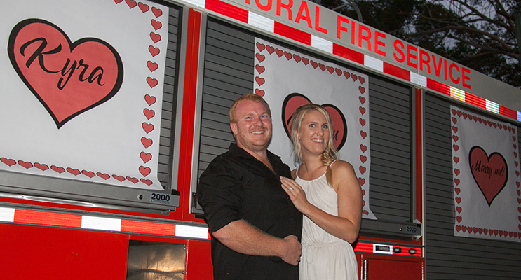 Harrison and Kyra in front of a brigade truck emblazoned with ‘Kyra will you marry me”.