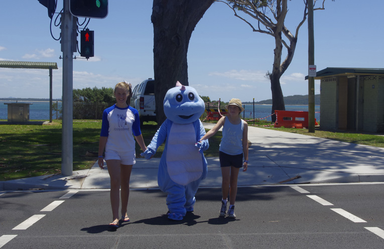 Lucy Hudson The Little Blue Dinosaur and Sophie McLaughlin (Tom’s older sister) crossing the road safely at Shoal Bay. Photo by Marian Sampson.